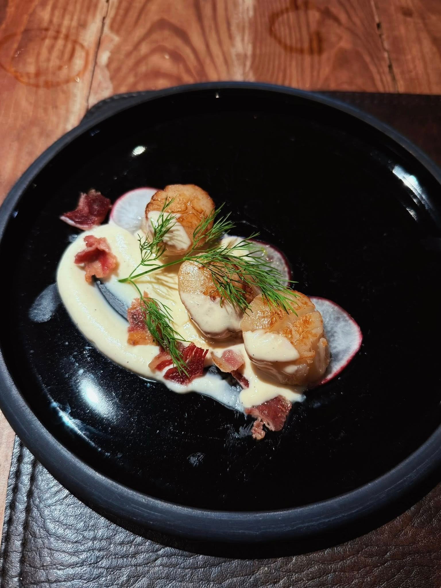 A dark plate of seafood with cream sauce and herbs.